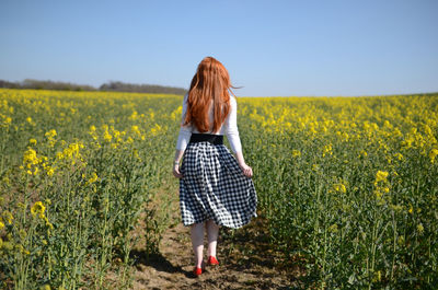 Full length rear view of woman walking in agricultural field against clear sky