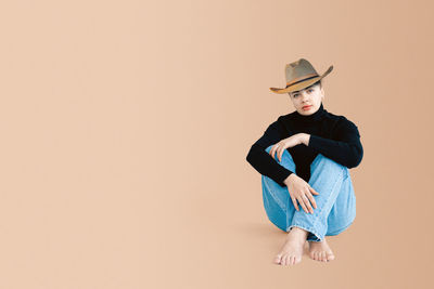 Portrait of young woman wearing hat sitting against gray background