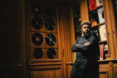 Bearded man with arms crossed standing by cabinet 