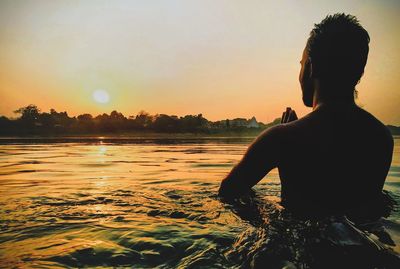 Silhouette man looking at sea against sky during sunset