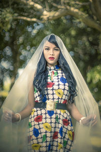 Portrait of a beautiful young woman standing against tree
