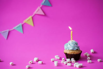 Lit candle on cupcake with bunting over pink background