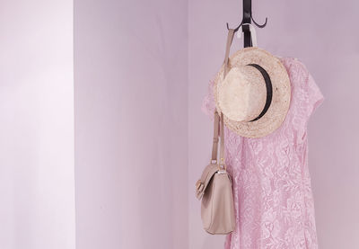 Dress with hat and purse hanging on coat hook against pink wall