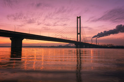 Suspension bridge over sea with industry in the background