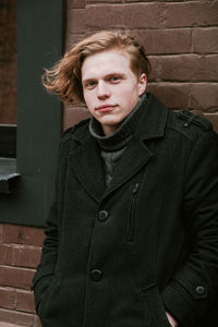 Portrait of young man wearing warm clothing while standing against wall
