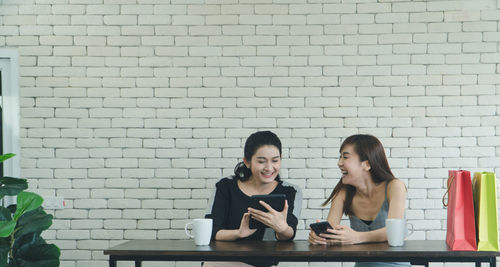 Young woman using mobile phone against brick wall