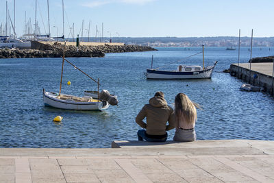 Rear view of people sitting on sea against sky