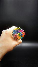 Close-up of hand holding multi colored pencils over black background