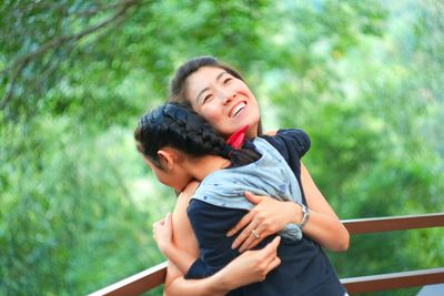 Smiling mature woman embracing daughter by railing