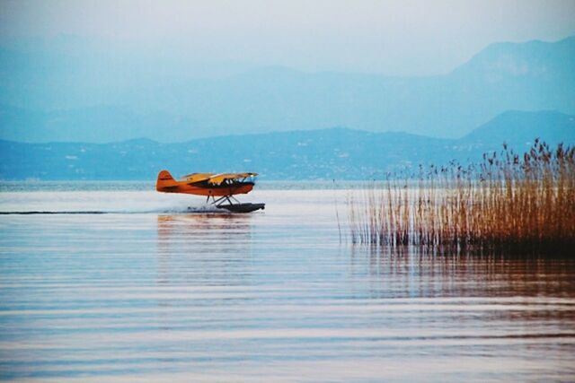 MAN IN BOAT ON WATER AGAINST MOUNTAIN