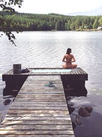 Woman doing yoga naked on wooden jetty in lake