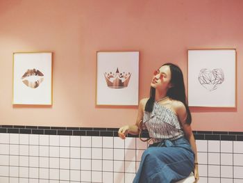 Young woman wearing sunglasses while sitting against wall