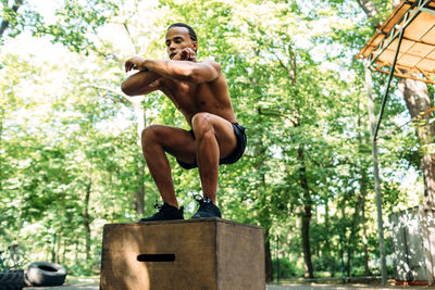 Full length of shirtless man exercising against trees