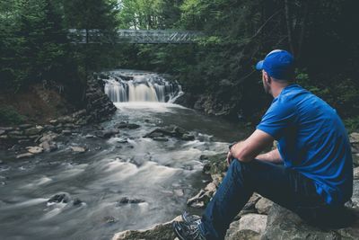 Man sitting on rock against waterfall in forest