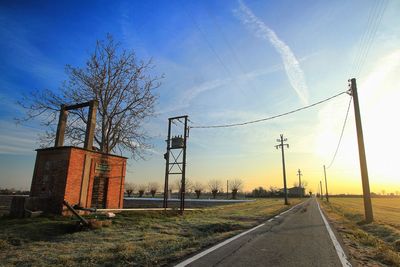 Road by electricity pylon against sky