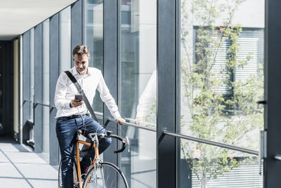 Businessman with cell phone on bicycle in office passageway