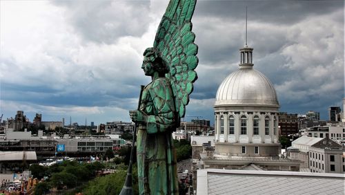 Statue in city against cloudy sky