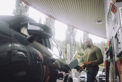 Mature man refueling vehicle while standing at gas station