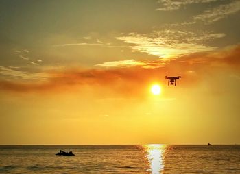 Silhouette drone over sea against sky during sunset