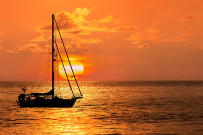 Silhouette sailboat in sea against sky during sunset