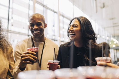 Happy female entrepreneur laughing while having smoothie with business professionals at convention center