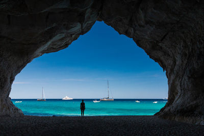 Silhouette woman standing in cave at beach against sea and sky