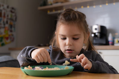 Little child girl sitting at the table and putting spoon at her mouth 