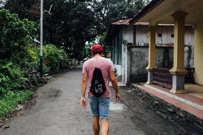 Rear view of man walking on road by houses