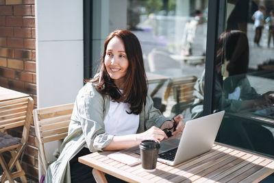 Adult smiling brunette business woman forty years in stylish shirt working on laptop in cafe 