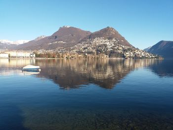 Scenic view of lake and mountains against clear blue sky
