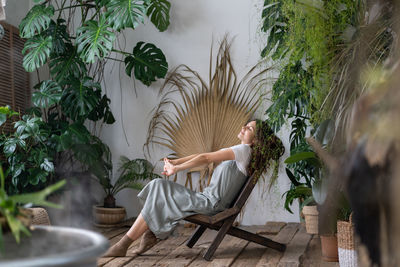 Dreamy woman relaxing in tropical resort-style garden at home, female gardener resting in greenhouse