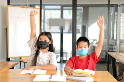 Asian girl boy student wearing face mask studying raising hand in classroom. learning education 