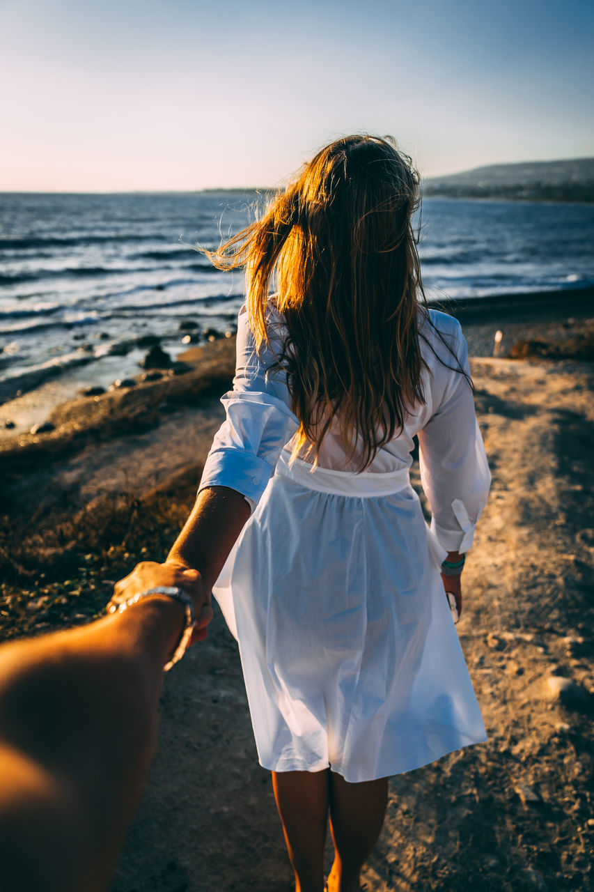 sea, real people, land, leisure activity, beach, women, lifestyles, sky, water, nature, two people, rear view, human hand, adult, people, horizon, hand, horizon over water, beauty in nature, hairstyle, outdoors