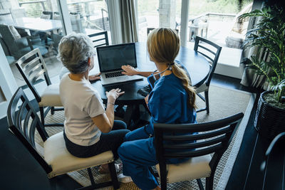 High angle view of home caregiver discussing over laptop computer with senior woman at dining table