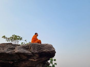 Low angle view of man sitting on rock against clear sky