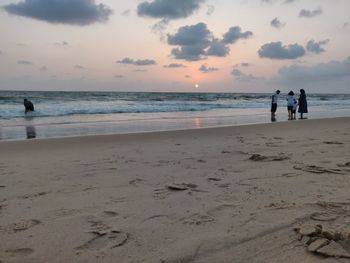 People on beach against sky during sunset