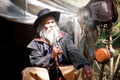 Man holding gun while sitting against hut