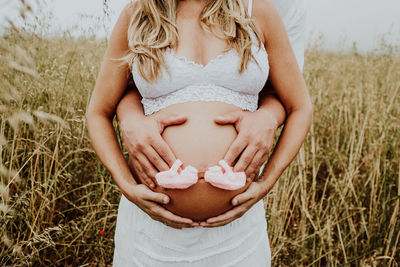 Midsection of husband embracing pregnant woman on grass field