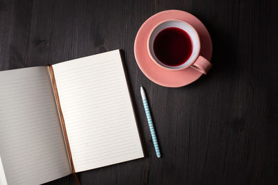 Open planer, a cup of pomegranate tea, a pen on a black wooden background