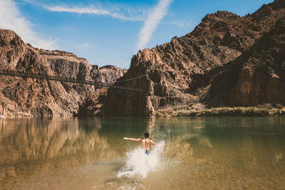 Scenic view of lake by mountains with man splashing water while running against sky