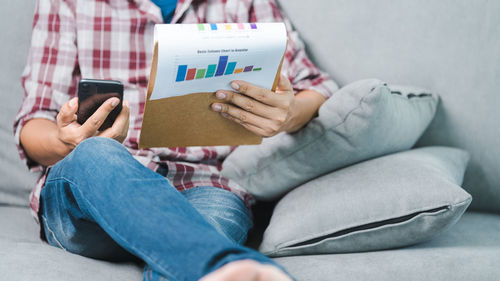 Midsection of man using mobile phone while sitting on sofa