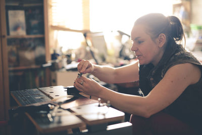 Girl master processes the metal copper plate on the workbench in the home workshop, soft focus 