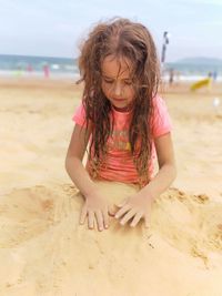 Girl playing with sand at beach against sky