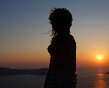 Woman standing by sea against sky during sunset