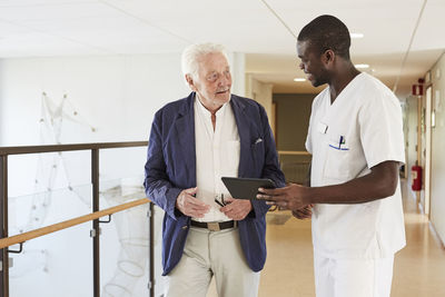 Male nurse and senior male patient discussing over digital tablet at hospital corridor