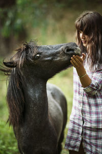 Loving woman stroking horse while standing on grassy field