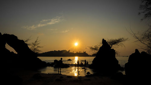 Silhouette people on beach against sky during sunset