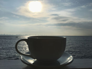 Coffee cup on table by sea against sky