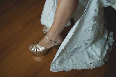 Low section of bride wearing sandals on hardwood floor