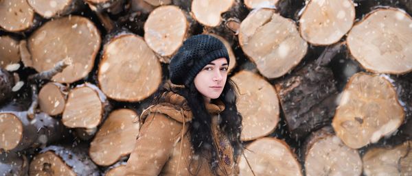 Portrait of young woman standing against firewood